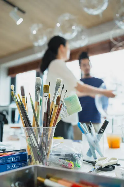 Art supplies in focus with blurred figures background, capturing a creative studio ambiance in Shinjuku, Tokyo.
