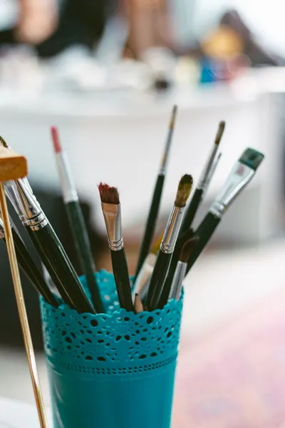 Close-up of various paintbrushes in a decorative blue holder, symbolizing creativity.