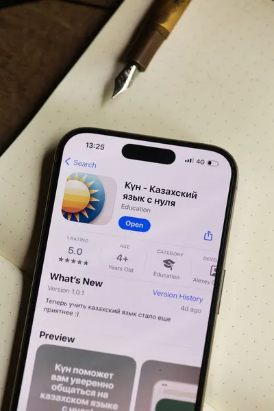 Close-up of a smartphone showing a Kazakh language learning app on a desk with a notepad and pen.
