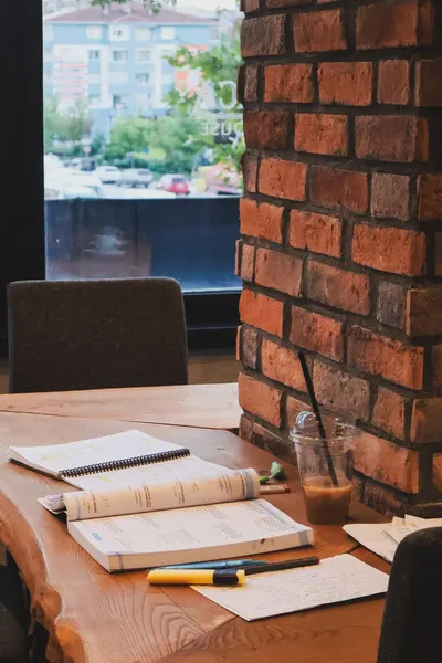 Inviting workspace with books, coffee, and rustic brick wall in a lively café setting.