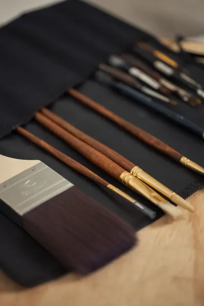 Close-up of various paintbrushes in a fabric holder, essential for artists.