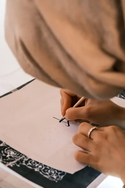 A woman carefully creates calligraphy on paper, showcasing artistic skill and focus.