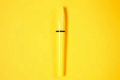 Minimalist yellow mascara tube displayed on a vibrant yellow background.