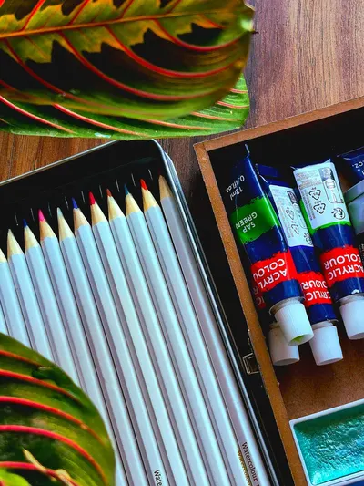 Colorful pencils and paints creatively laid out on a wooden surface with leaves.