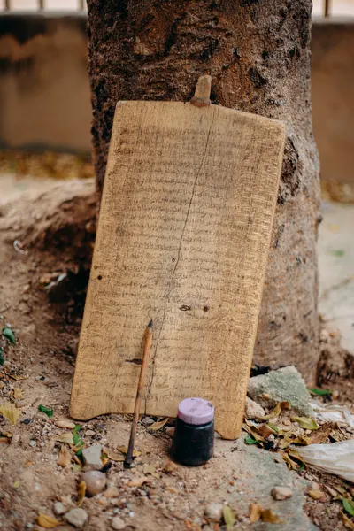 A wooden writing board with a pen and ink set against a tree outdoors.
