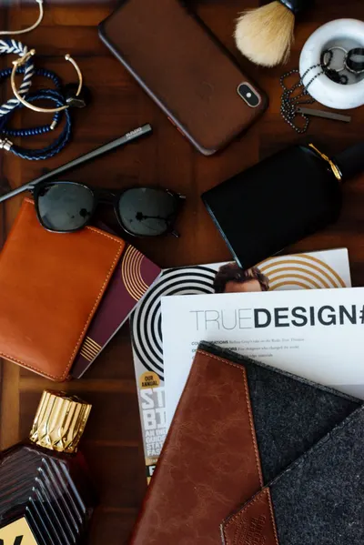 Sophisticated assortment of men's accessories including a phone, wallet, sunglasses, and magazines on a wooden desk.