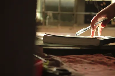 A hand reaching for a pen on a book by a sunlight window, evoking study and concentration.
