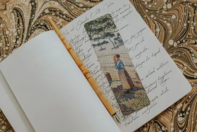 An artistic bookmark on a vintage notebook with handwritten text on a marble-patterned background.