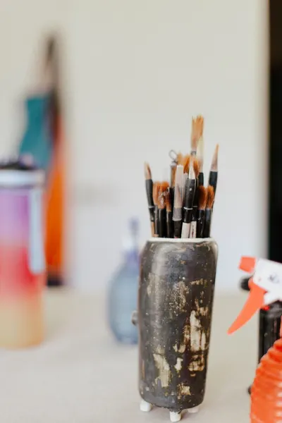 A collection of paintbrushes neatly arranged in a rustic ceramic holder on a creative workspace.