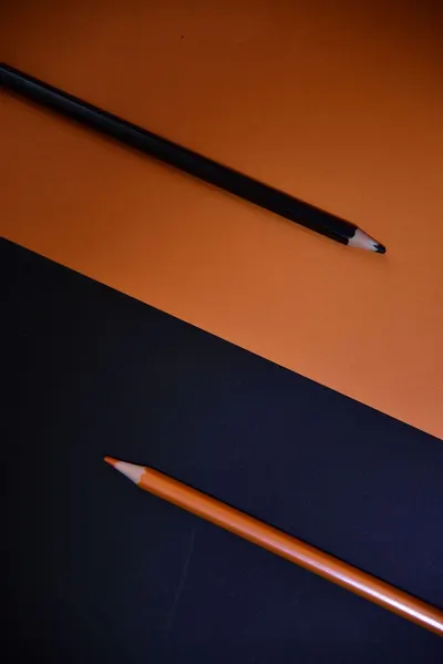 Artistic composition featuring black and orange pencils on a contrasting paper background.