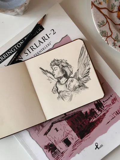 Sketch of an angel on notebook over a book, artistic and serene setting.