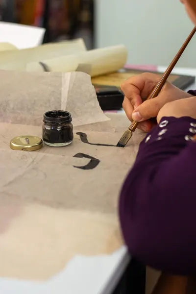 Close-up of hand creating calligraphy with brush and ink jar on paper.