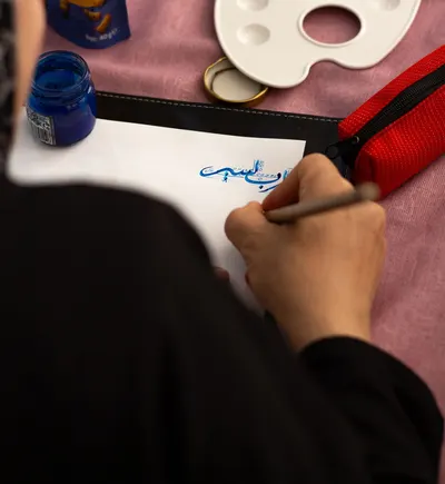 Close-up of a person practicing blue ink calligraphy indoors.
