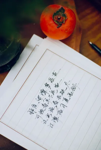 Handwritten Chinese poem beside a ripe persimmon on a wooden table.