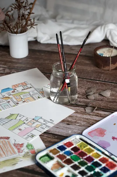 Engaging creative setup with watercolor paints, sketches, and brushes on a wooden table.