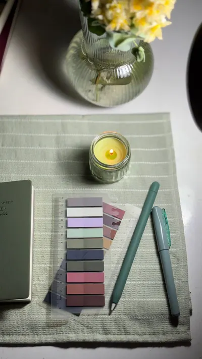 Elegant desk setup with pastel pens, candle, and flowers on a light green mat.