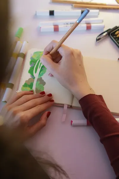 Creative artist drawing a tree illustration in a sketchbook using colored markers.