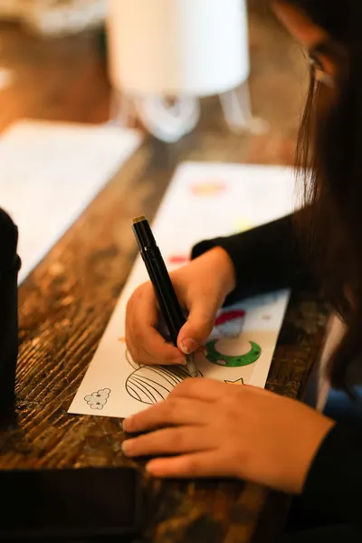 Woman engaged in an art project, drawing with precision and creativity indoors.