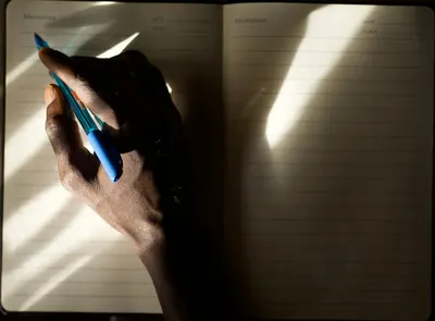 An individual writes notes in a lined notebook, captured in dramatic light and shadow.