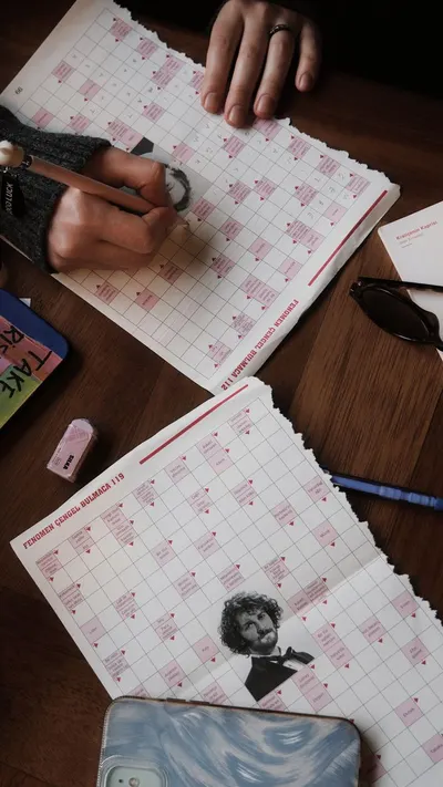 Overhead view of hands writing on calendars with pencils, featuring glasses and erasers on a wooden table.