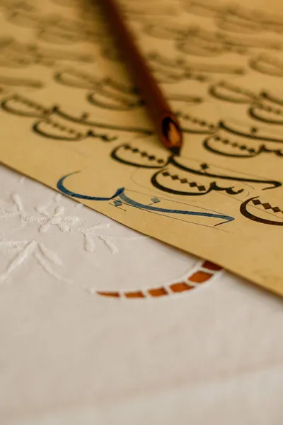 Close-up of Arabic calligraphy practice with a pen on textured paper.