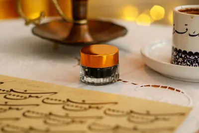 Elegant setup of calligraphy writing with ink pot and Arabic coffee cup on a decorative table.