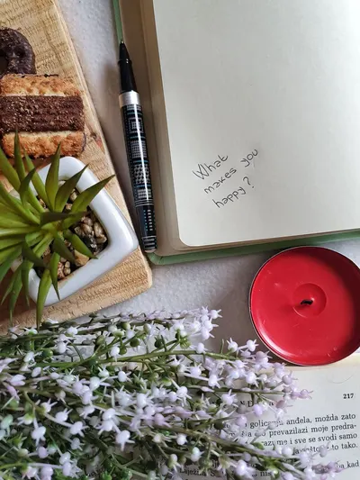 Top view of opened copybook with bright candle and bunch of flowers near board with cookies on table
