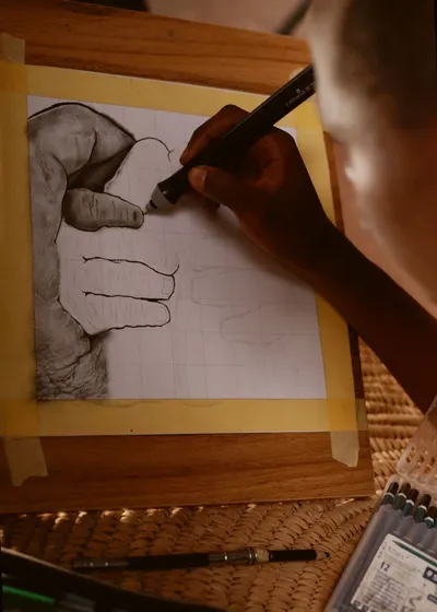 Close-up of an artist sketching a hand on paper using a charcoal pencil, showcasing detailed artistry.