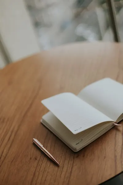 An open notebook and pen on a wooden table, perfect for creativity and journaling.