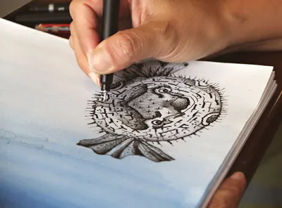Close-up of a hand drawing a detailed pufferfish sketch with a pen on paper.