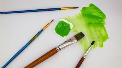 Top view of paintbrushes and green watercolor paint on canvas.