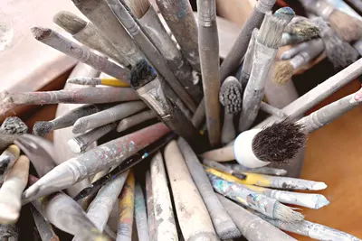 A collection of paintbrushes with colorful paint residue in an artist's studio.