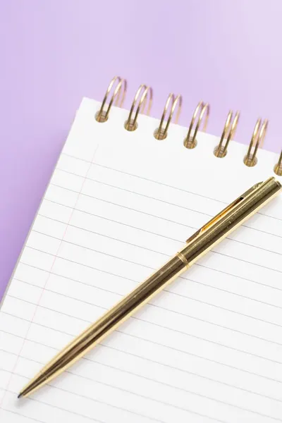 Gold pen on a spiral notebook with a purple background, perfect for note-taking aesthetics.