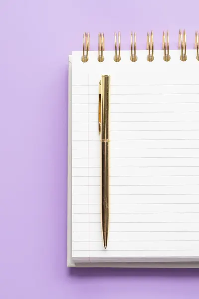 Gold pen on lined notebook with purple background, perfect for stationery themes.