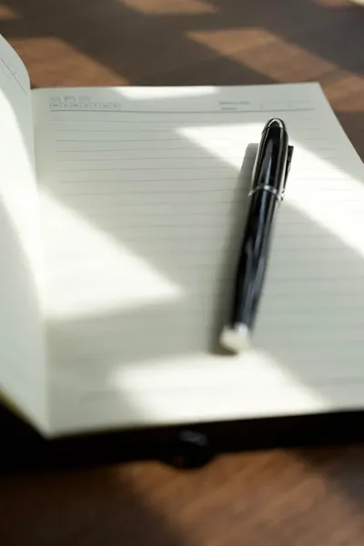 Open notebook with black pen under warm sunlight creating artistic shadows.