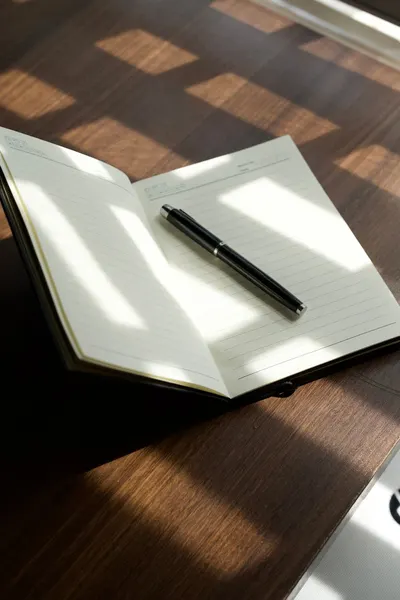 An open notebook with a pen on a sunlit desk, showcasing a minimalist workspace.