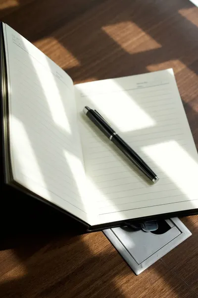 Open notebook with a pen on a wooden desk under soft light, offering a classic workspace ambiance.