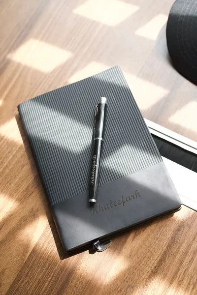 A sleek black journal with a pen on a sunlit wooden desk, offering a professional vibe.