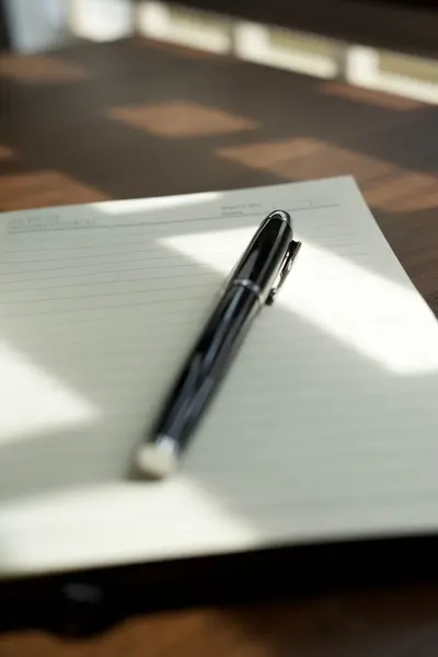 A sleek pen rests diagonally on a lined notepad, illuminated by soft sunlight.