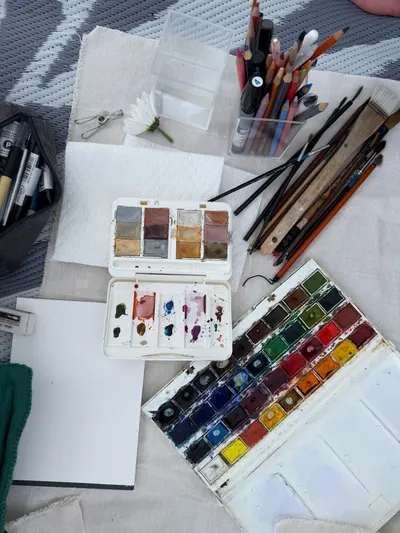 Top view of art supplies including watercolors, brushes, and pencils on a textured surface.