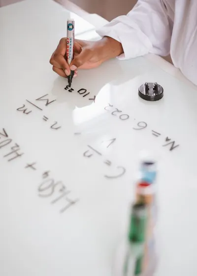 Unrecognizable ethic chemist in uniform writing with marker formulas on whiteboard after analysis chemical reaction on test tubes in laboratory
