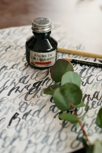 Close-up of calligraphy ink bottle with foliage on script paper, enhancing artistic ambiance.