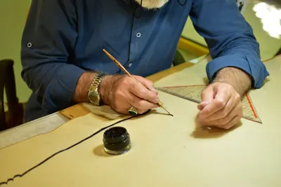 Artisan using a dip pen and ink to create a detailed design on paper, showcasing craftsmanship.