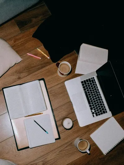 Overhead shot of a cozy workspace with a laptop, notebooks, and coffee.