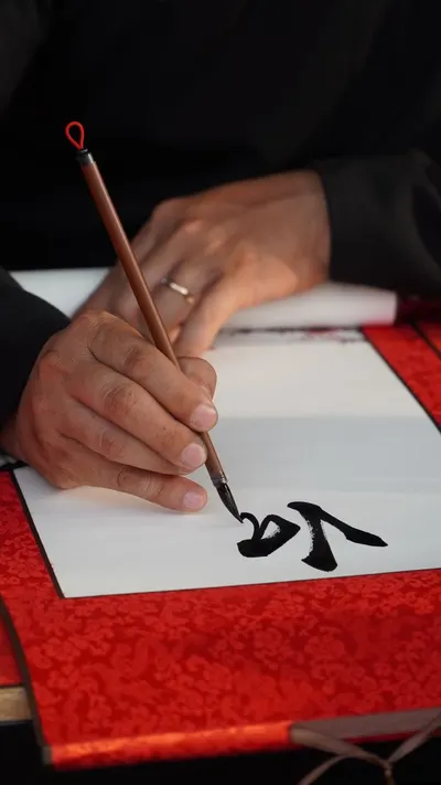 Close-up of hand writing calligraphy with brush on decorative paper, focusing on artistic detail.