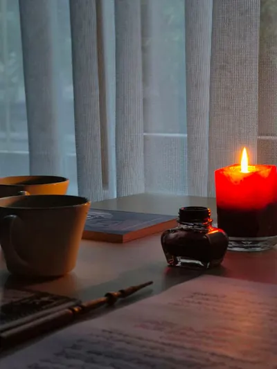 Warm and inviting writer's nook featuring a lit red candle, ink bottle, and writing materials.