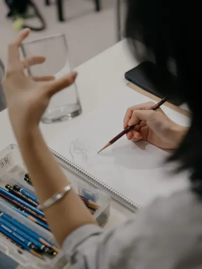Close-up of an artist drawing in a sketchbook while holding a glass, showcasing creativity.