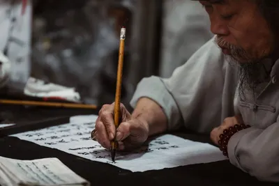 An elderly Vietnamese man focused on traditional calligraphy with a brush pen.
