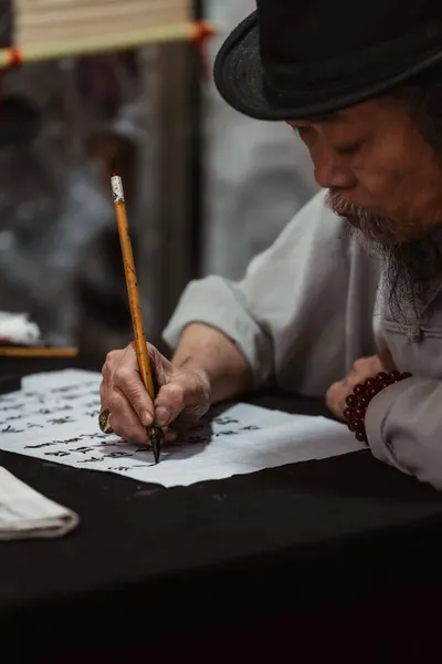 Elderly artist practicing traditional Vietnamese calligraphy indoors.