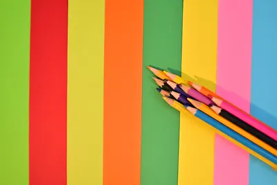 Top view of a rainbow of colored pencils on brightly colored paper sheets.